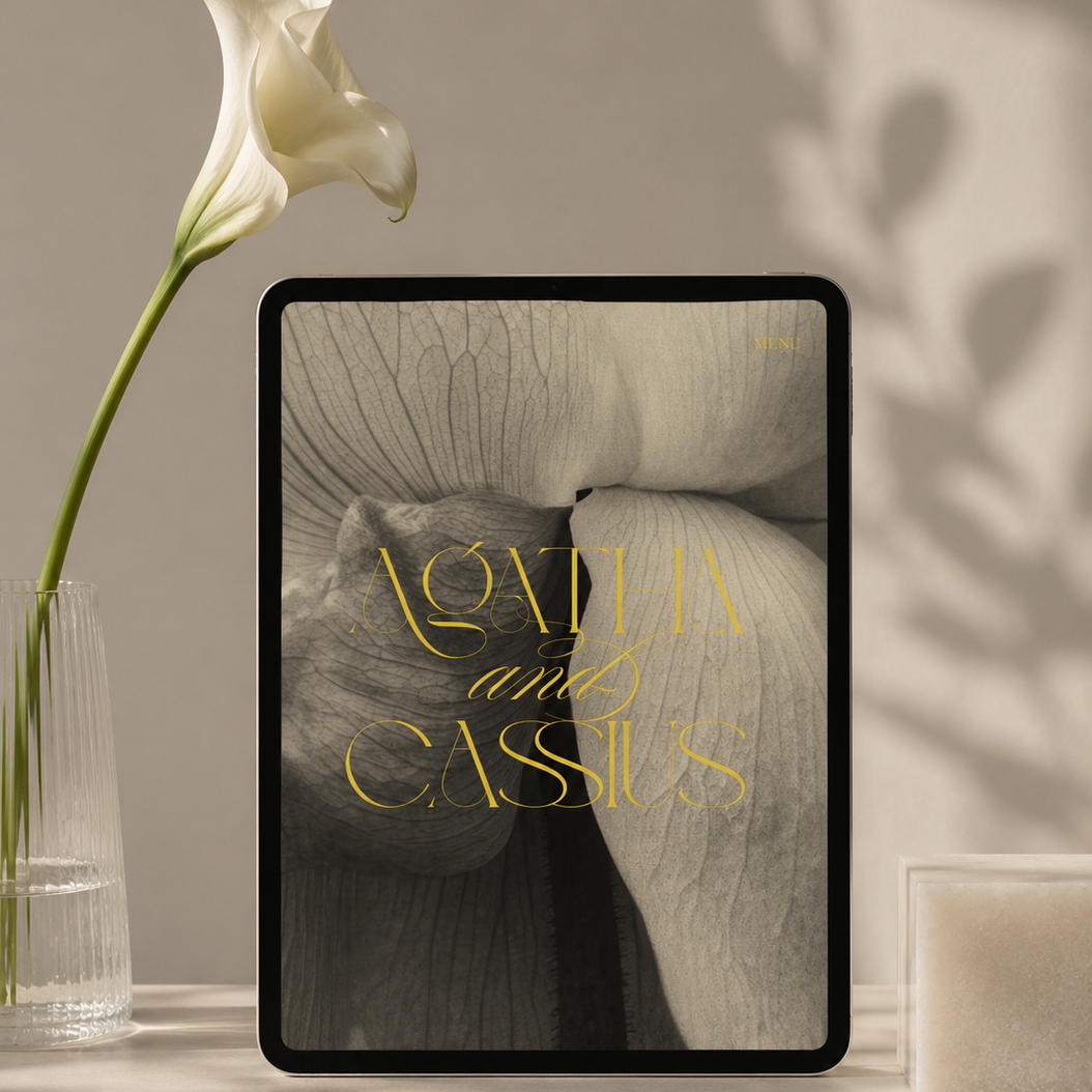 iPad displaying a modern wedding website for Agatha and Cassius, styled with elegant gold typography and floral photography, beside a white calla lily in soft natural light.