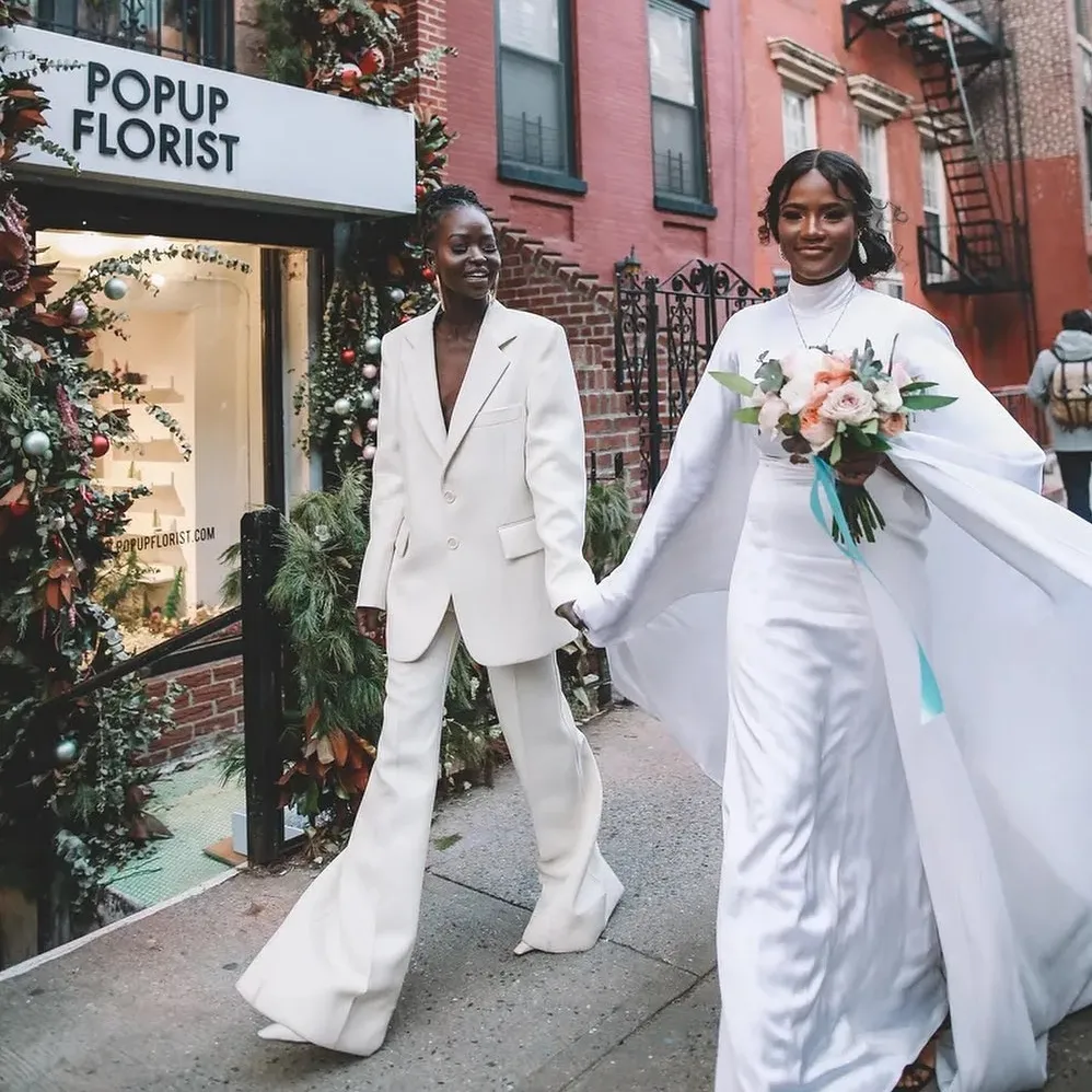 LGBTQ weddings: LGBTQ wedding couple holding hands walking down the street in front of a popup florist shop