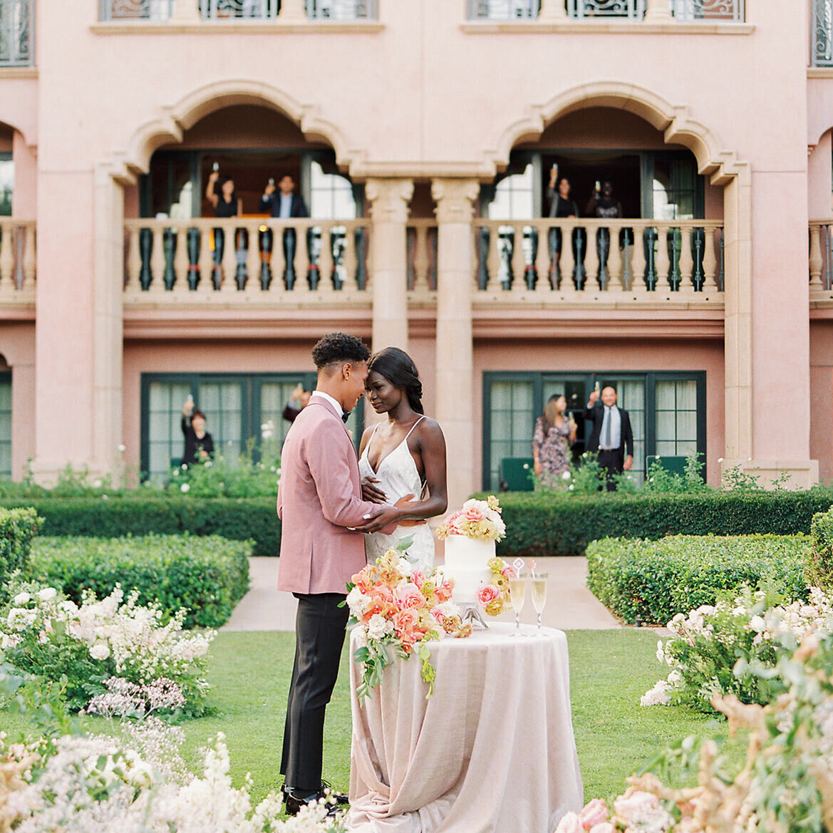 2022 Weddings Survey: A couple embracing with their wedding guests cheering from the building behind them.