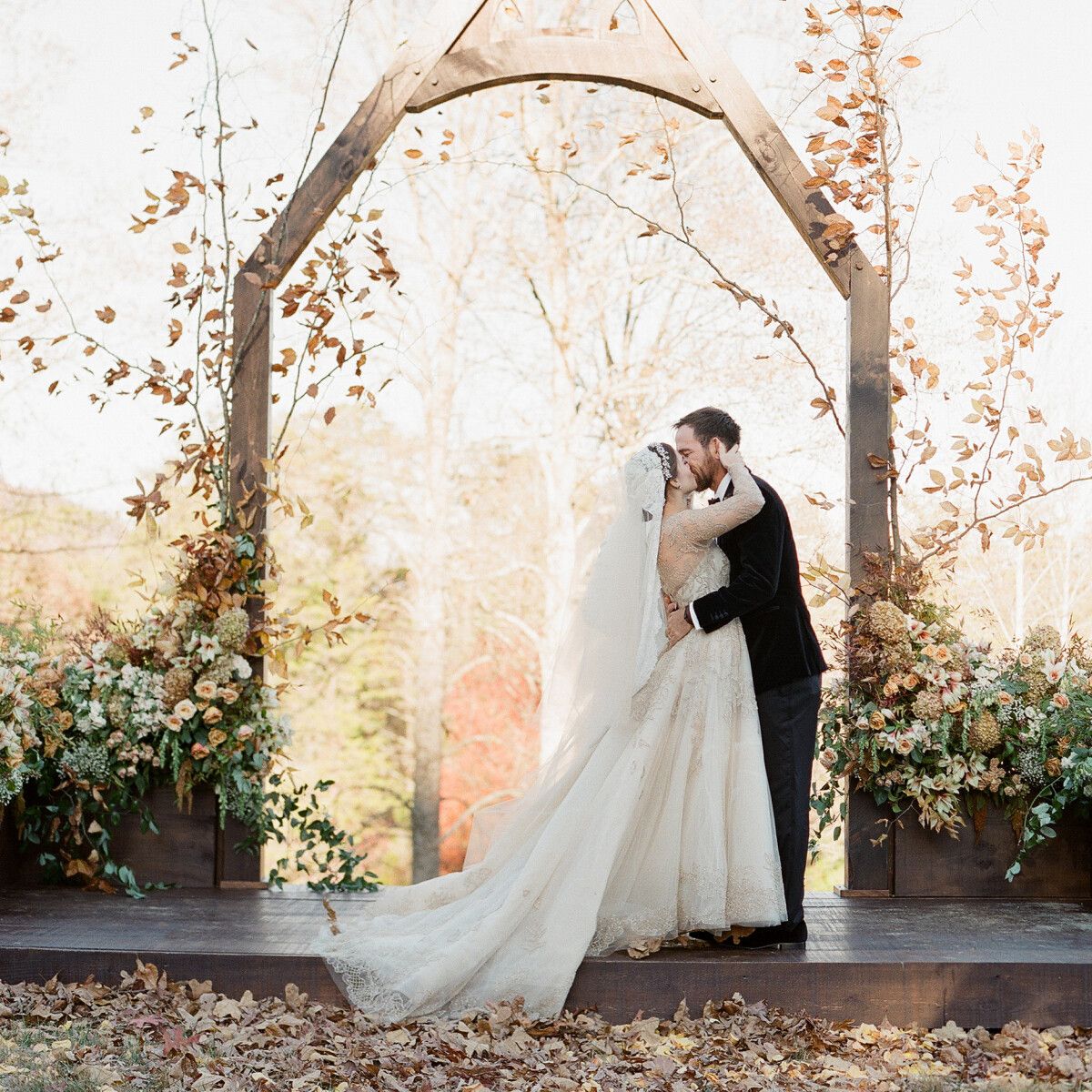 Wedding couple kissing at fall foliage inspired wedding arbor