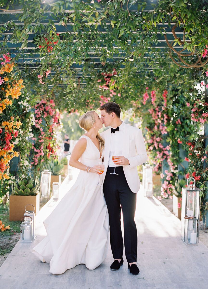 Groom in white jacket tuxedo groom attire posing with bride in a garden pathway