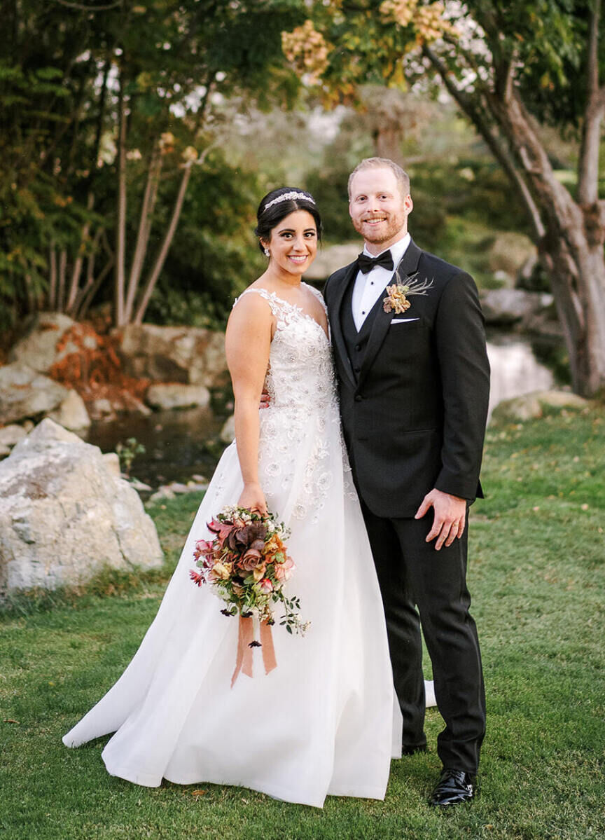 A bride wearing a low updo and headband poses with her groom at their earth tone wedding in California.