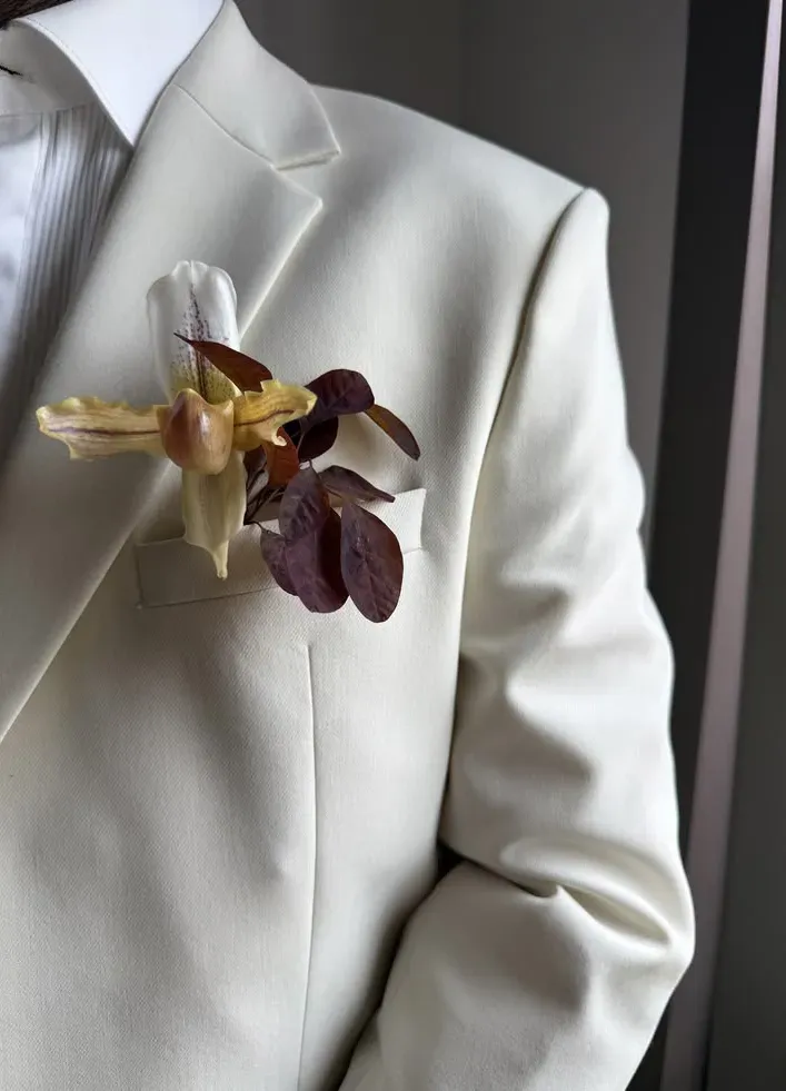 Ivory tuxedo with an orchid and copper-leaf boutonnière, close crop.