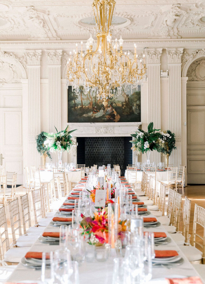 Castle Wedding Venues: An indoor reception setup with a long table featuring red place settings and a gold chandelier hanging above.