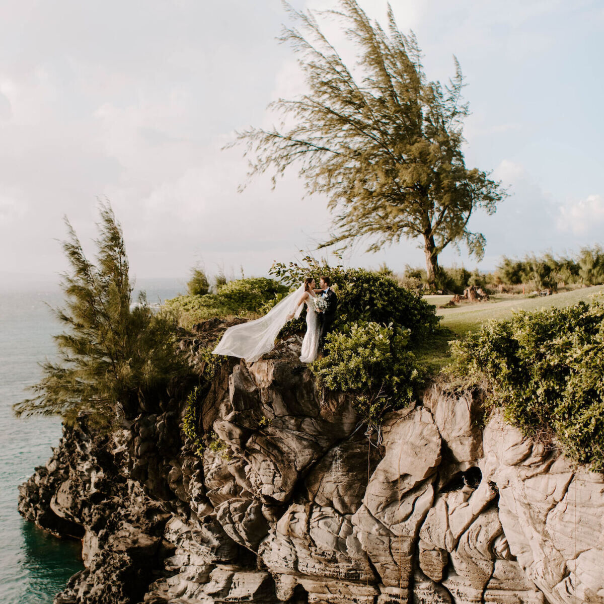 A bride and groom standing on the edge of a cliff at The Ritz-Carlton Maui, Kapalua in Kapalua, Hawaii.