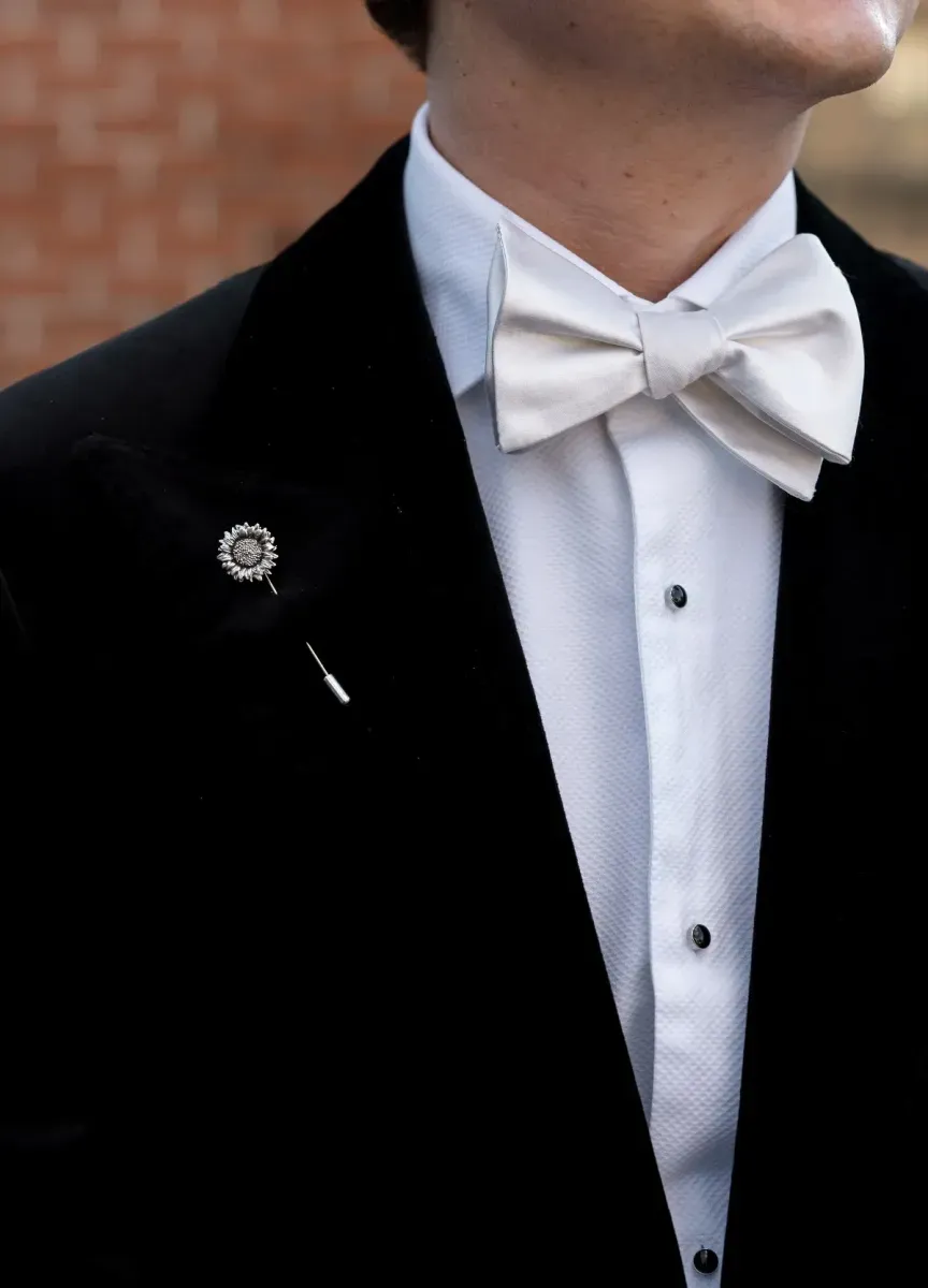 An up-close look at a groom with a white bow tie and tuxedo with a pin on the lapel.