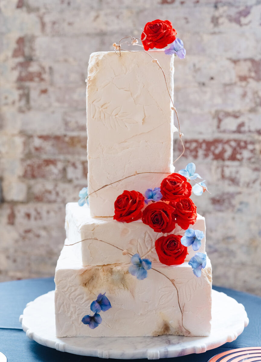 A three-tier wedding cake decorated with red and blue flowers and leaf impressions made a statement at an art museum wedding.