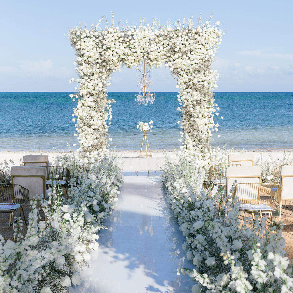 Beach wedding ceremony set up featuring wedding arch of all white blooms