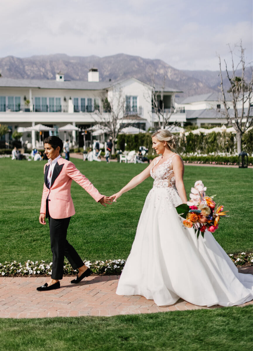 Wedding couple waling hand in hand along a garden path in front of an estate