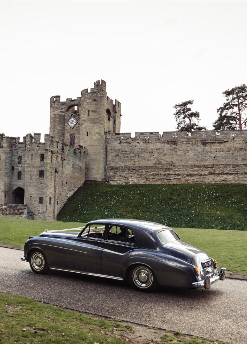 Castle Wedding Venues: An old fashioned car driving up to a stone castle in Warwick, England.