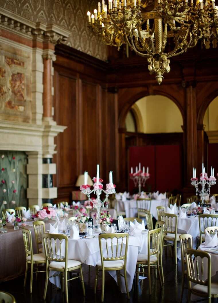 Castle Wedding Venues: Round tables with gold chairs and a gold chandelier for a reception at a castle in England.