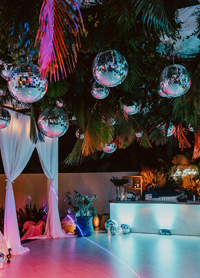 Ceiling Wedding Decor: Disco balls and palms hanging from the ceiling at a colorfully-lit reception area in Mexico.