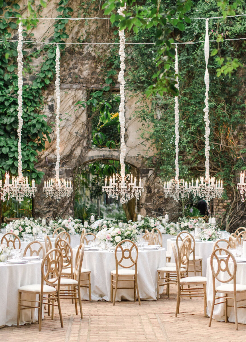 Ceiling Wedding Decor: Chandeliers hanging above at an outdoor reception with round tables in Maui.