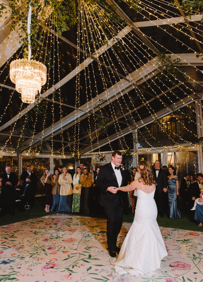 Wedding Ceiling Decor: A wedding couple dancing on a floral-patterned dance floor with string lights overhead.