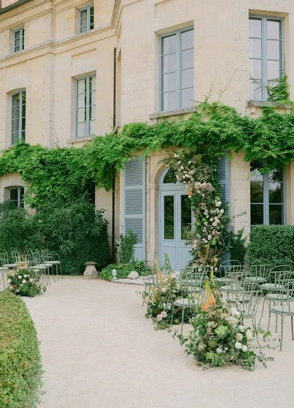 The exterior of a chateau in France, with French blue doors and shutters and lush greenery growing on the manor.