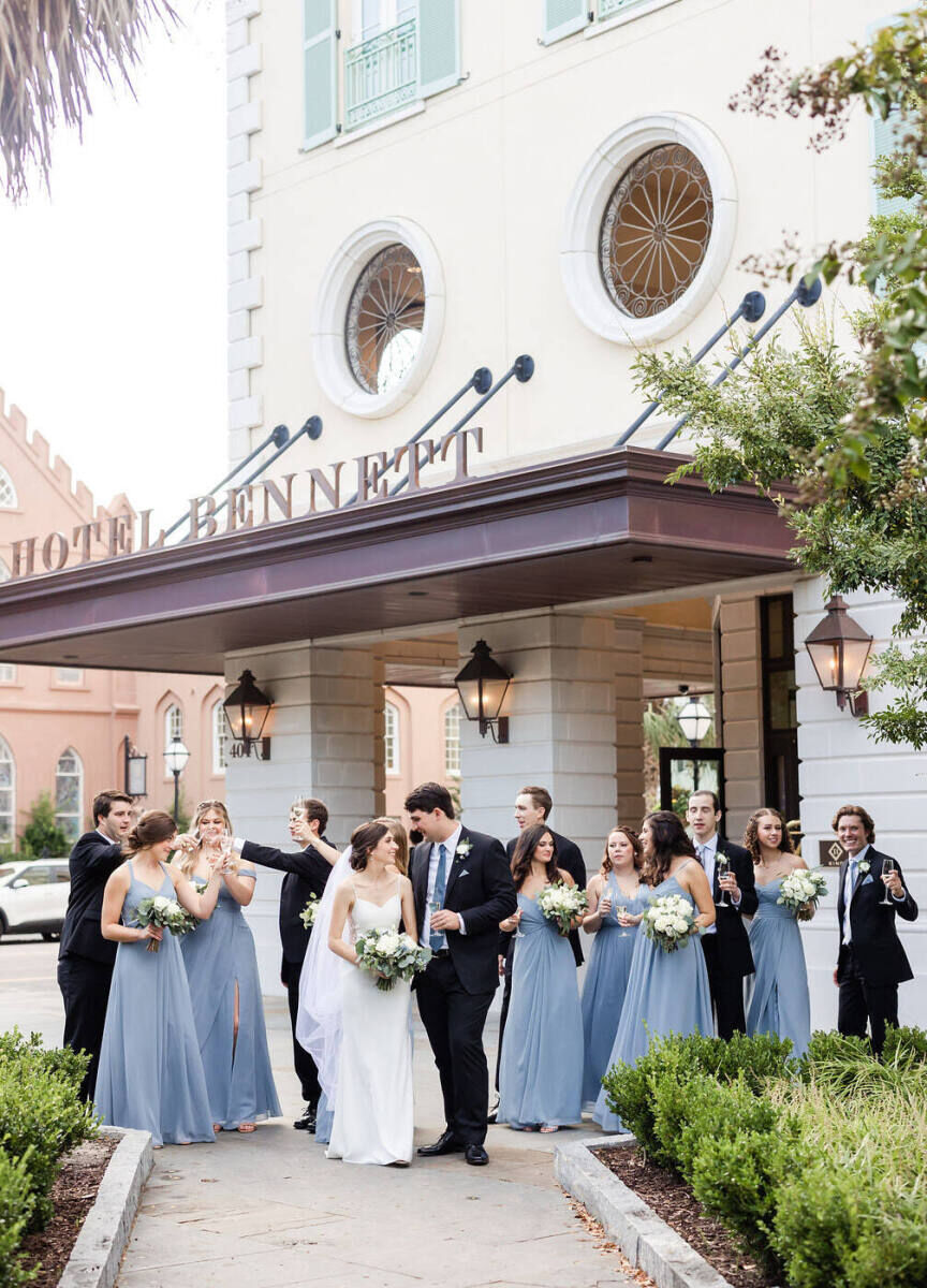 City Weddings: A wedding couple smiling at each other with the rest of their party outside of Hotel Bennett in Charleston.