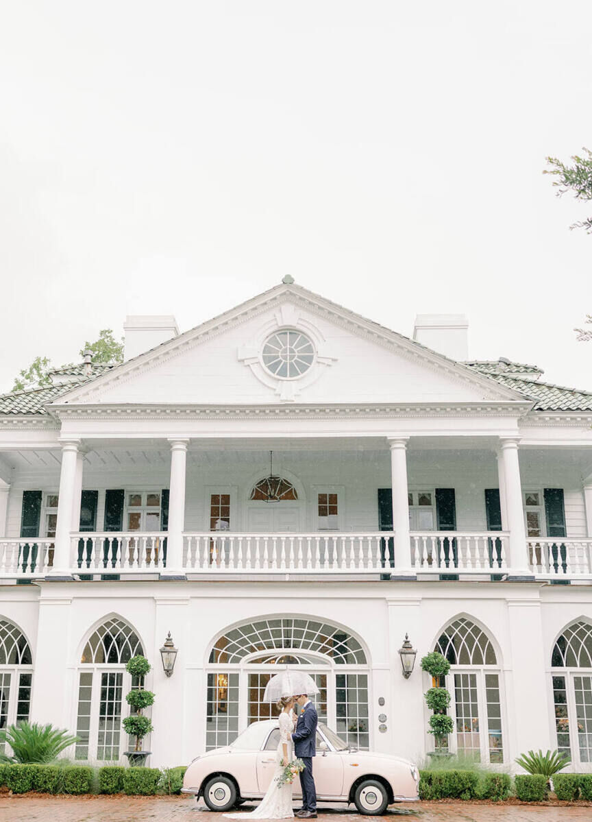 City Weddings: A couple facing each other while standing under an umbrella, next to an old fashioned car at an estate wedding venue in Charleston.