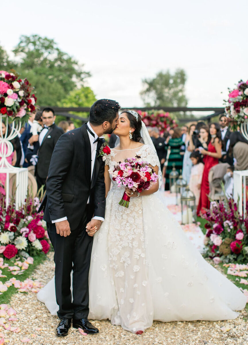 Newlyweds share a kiss at the end of their aisle at the end of their colorful countryside wedding ceremony.