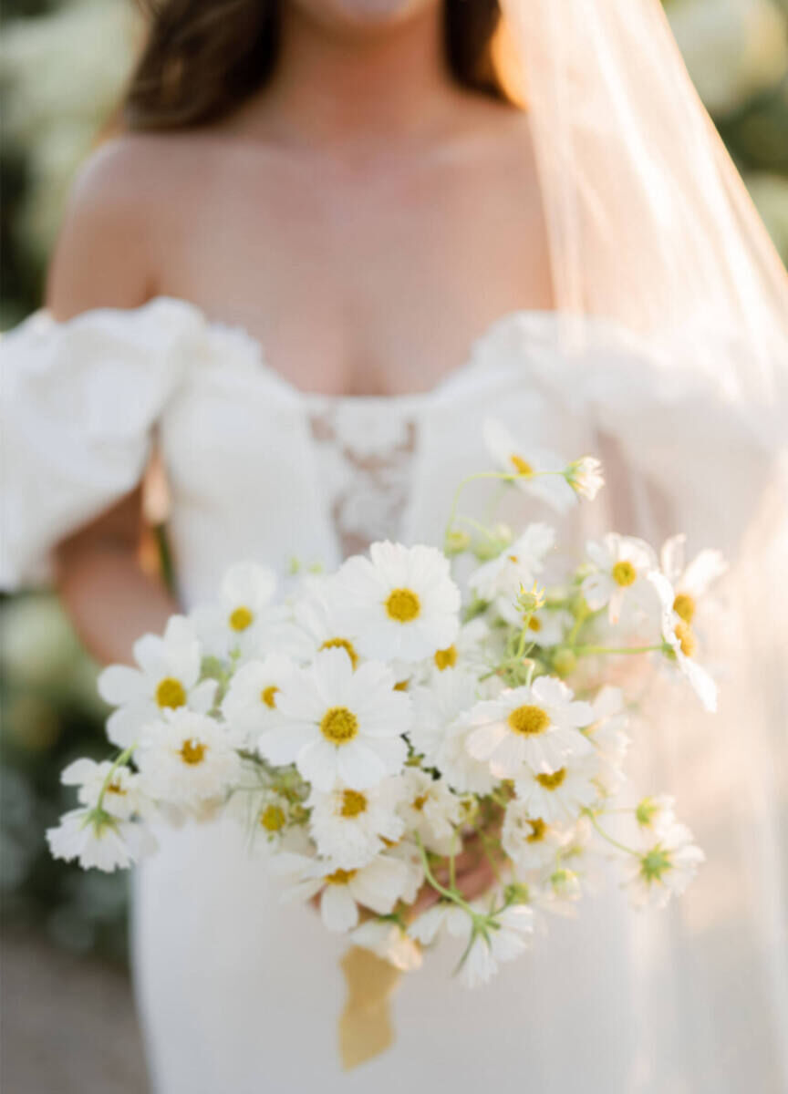 A bride holds her cottagecore wedding style bouquet, composed of single and double cosmos tied with silk ribbons.