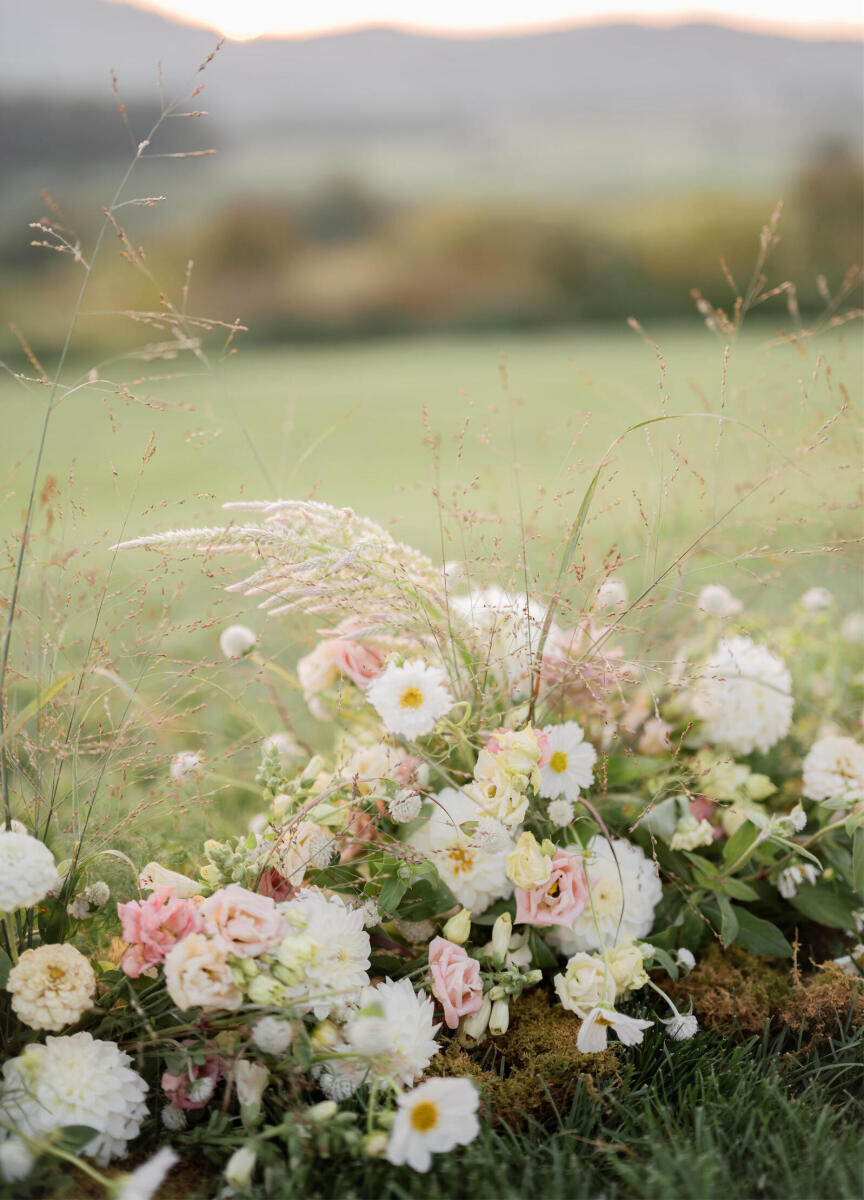 Low arrangements of flowers, grasses, and moss anchored the ceremony lawn at a cottagecore wedding in the Virginia countryside.