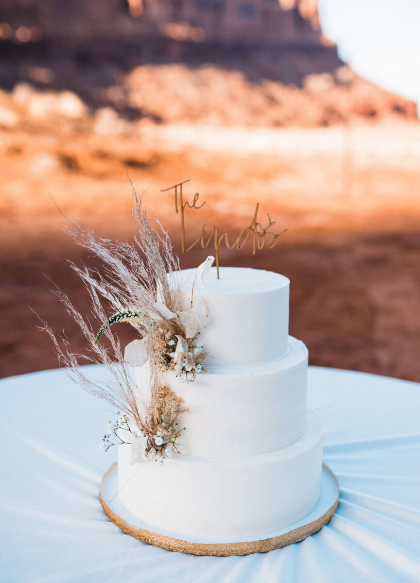 The cake at a desert wedding was decorated with some fresh flowers, wild grasses, and a cake topper with the couple's shared last name.