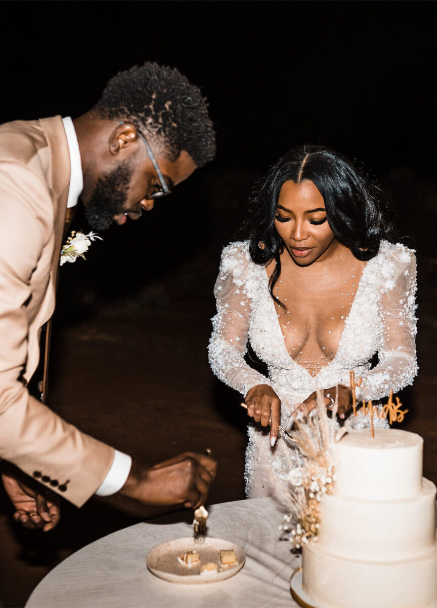 A couple cuts into and eats their wedding cake at their desert wedding.