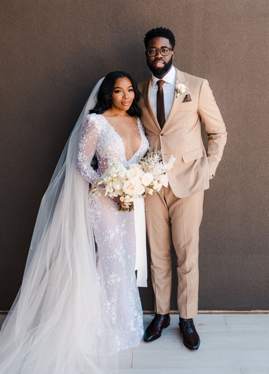 A bride and groom pose for a portrait ahead of their desert wedding in Utah. She holds a bouquet of white flowers, which match his simple boutonniere.