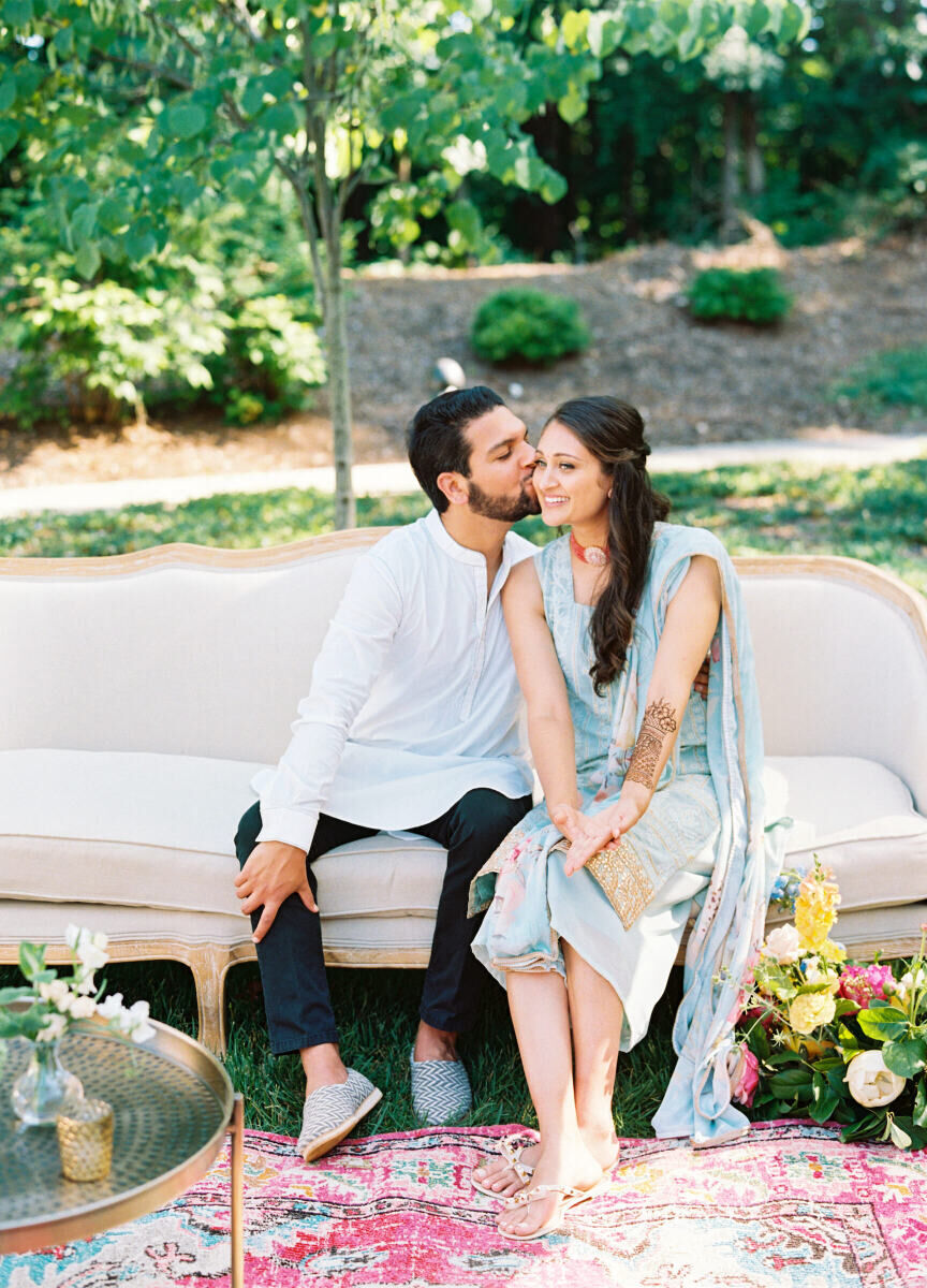 A groom kisses his bride while sitting in a beautiful lounge area during the mehndi portion of their destination Indian wedding weekend.