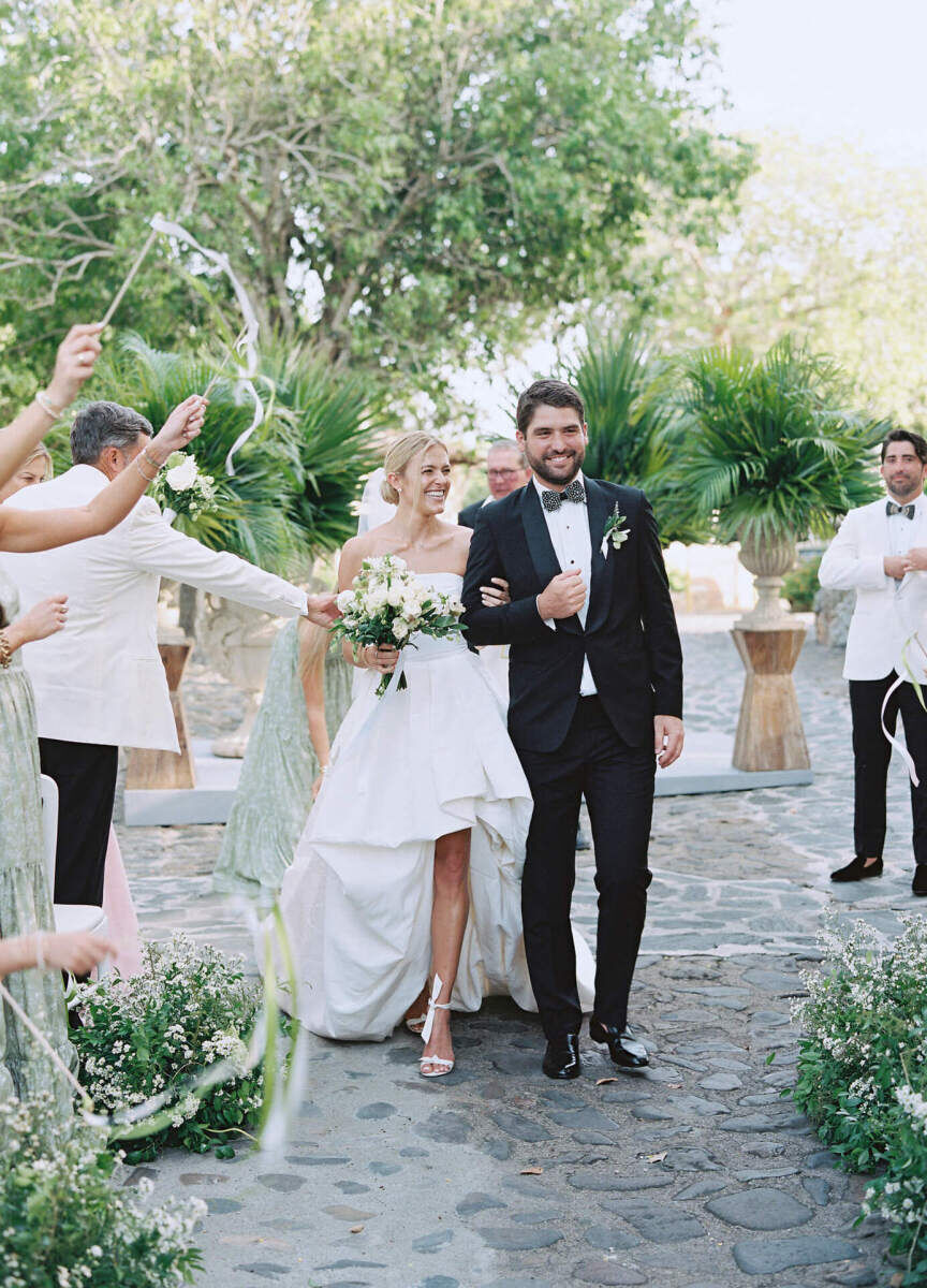 Newlyweds begin to recess up the aisle as their guests wave ribbon wands during the ceremony of their destination wedding.