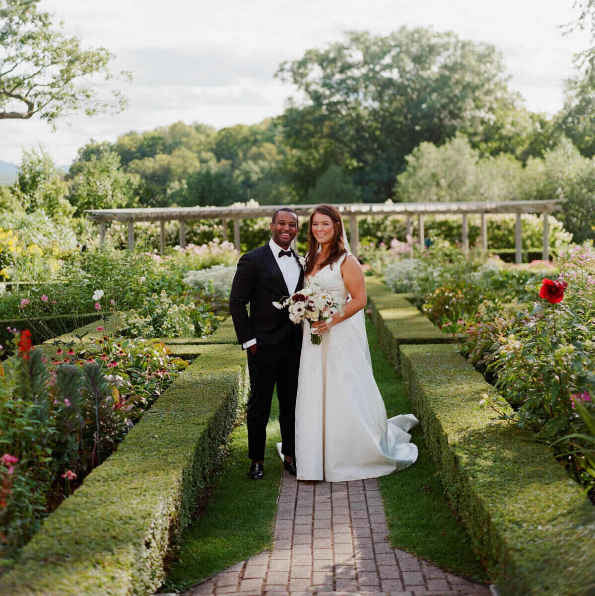 A groom and bride smile on the grounds of their Vermont wedding venue during their elevated garden wedding.