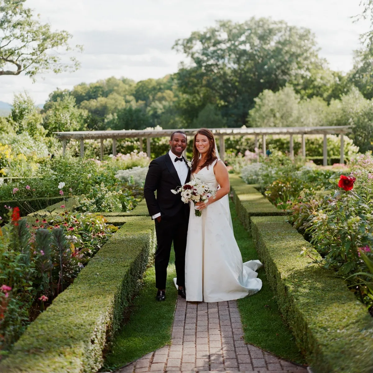 A groom and bride smile on the grounds of their Vermont wedding venue during their elevated garden wedding.