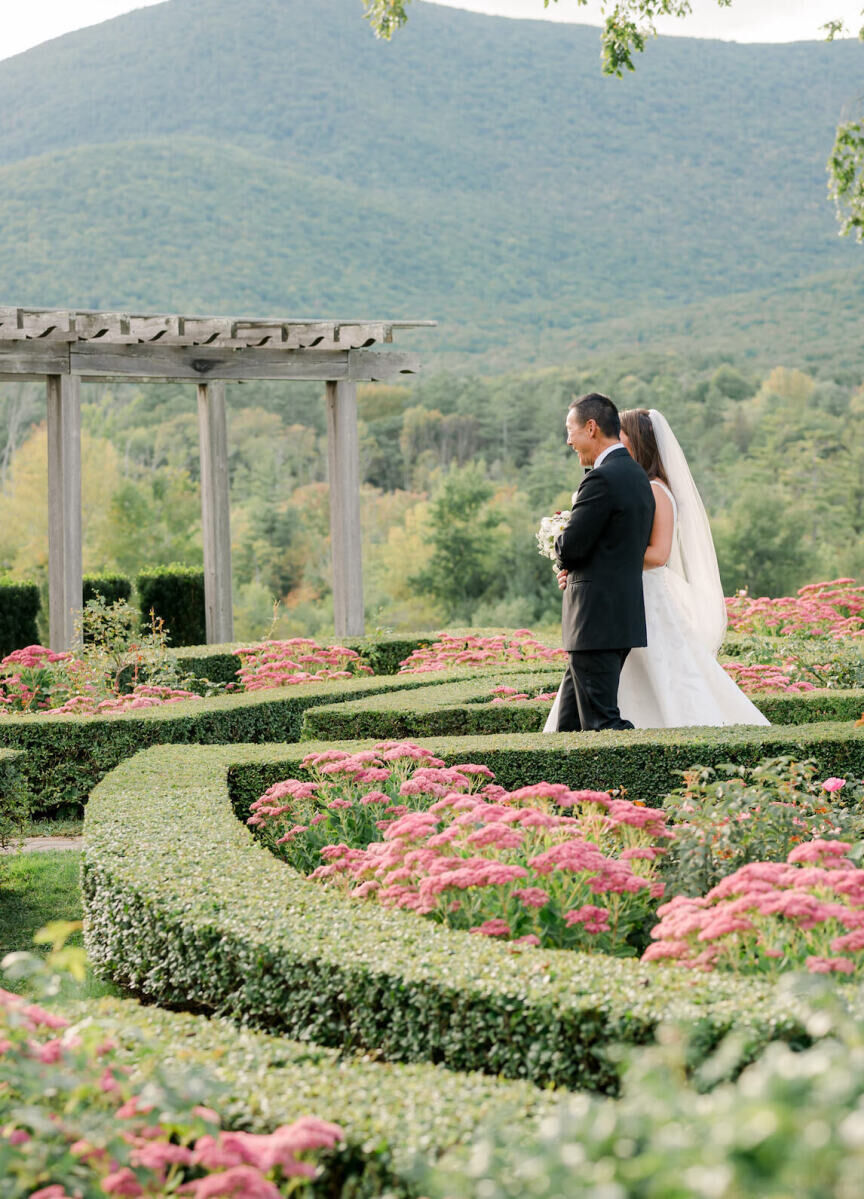 A bride and her father process through a manicured garden towards her elevated garden wedding ceremony.