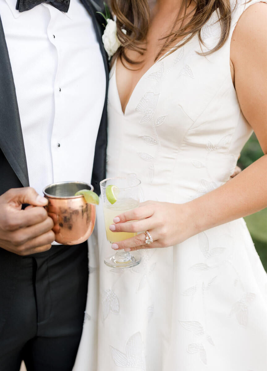 A groom and bride hold a pair of cocktails at their elevated garden wedding reception.