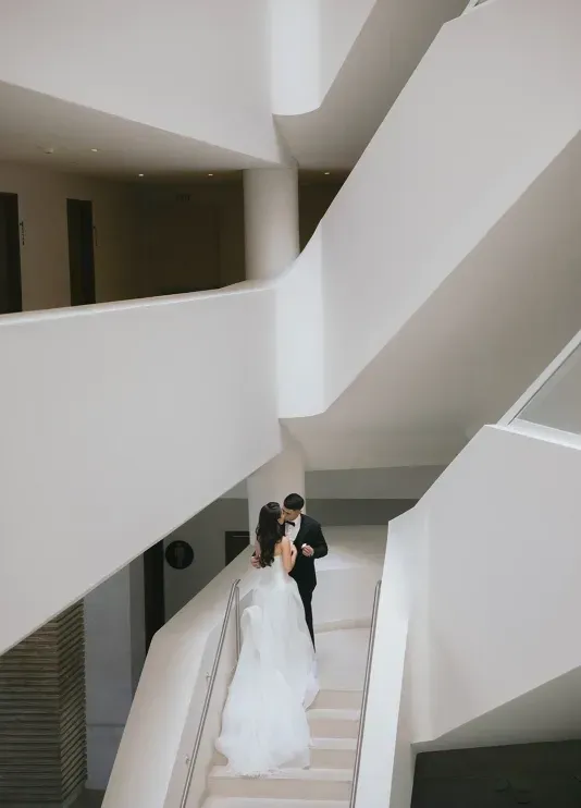 A wedding couple sharing a kiss on a white staircase at a modern wedding venue in Cabo San Lucas, Mexico. 