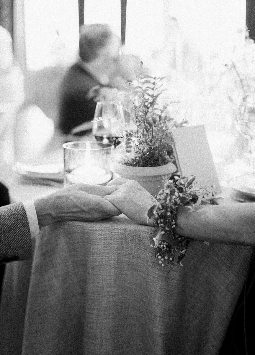 A man holds a woman's hand, while she wears a bracelet made of fresh greenery given to her during the ceremony of an enchanted waterfront wedding.