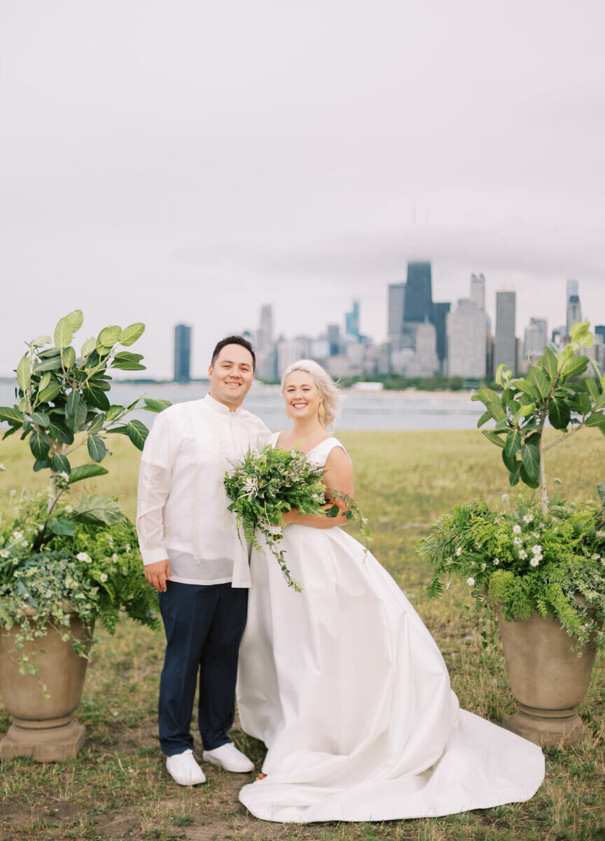 A groom and bride (who holds a bouquet of mostly greenery) smile for a portrait during their enchanted waterfront wedding, with views of Lake Michigan throughout the ceremony.