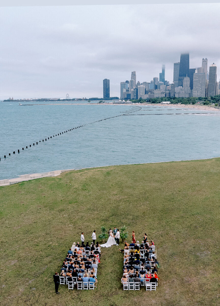 An aerial view of an enchanted waterfront wedding on Lake Michigan, with the skyline of Chicago in the distance behind the bride and groom.