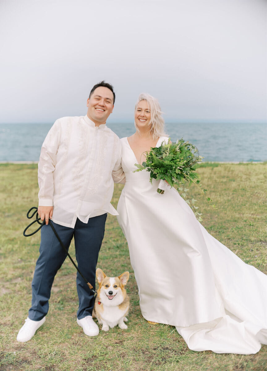 A groom and bride, and their corgi, smile after getting married in an enchanted waterfront wedding ceremony.