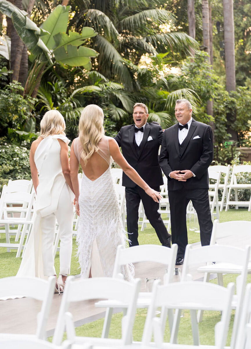 First Look Photos: Two brides and their dads sharing a first look in a tropical outdoor setting.