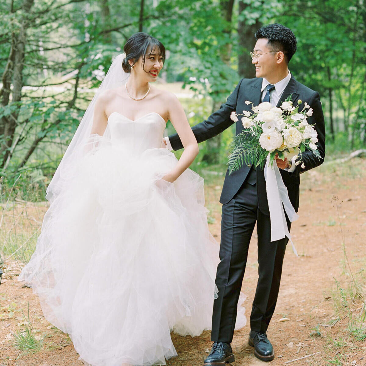 Newlyweds look at each other as they head through the woods for portraits at their forest wedding.