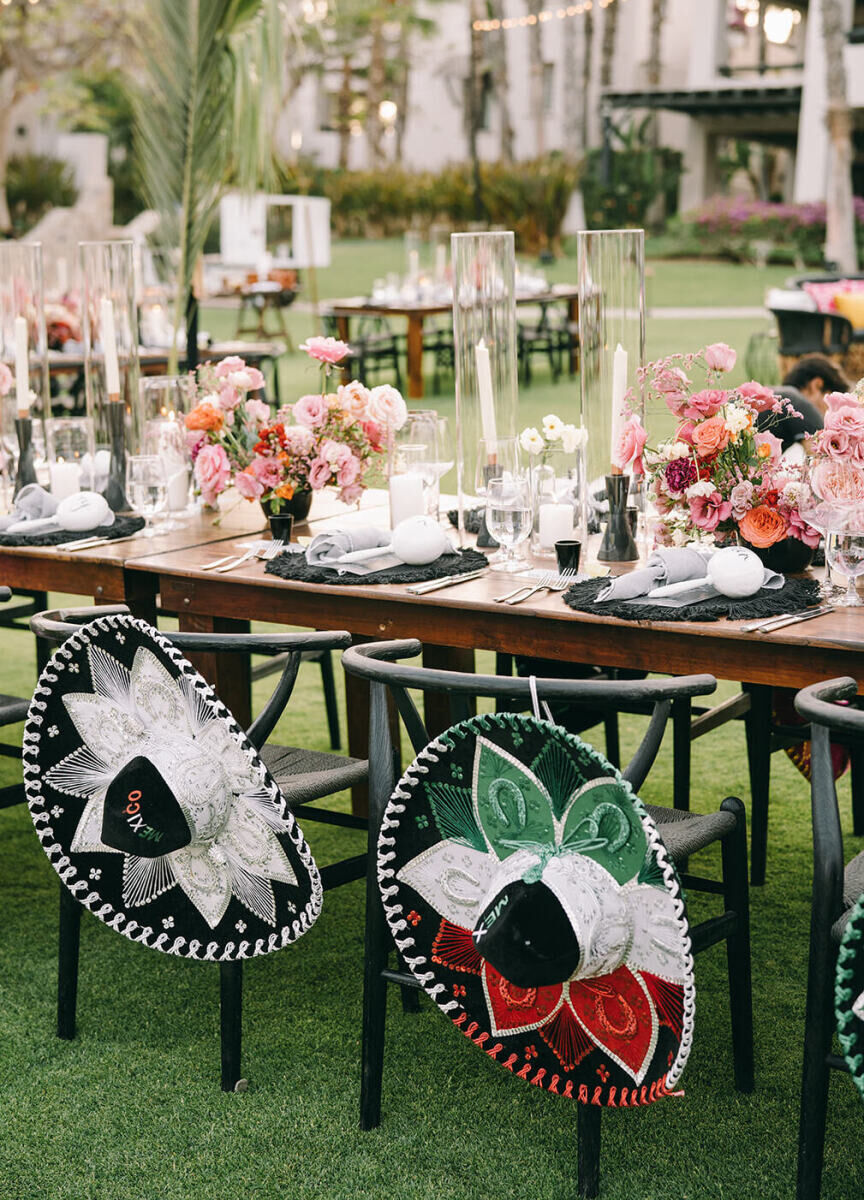 Sombreros hang from black wishbone chairs at a glam beach wedding reception in mexico.