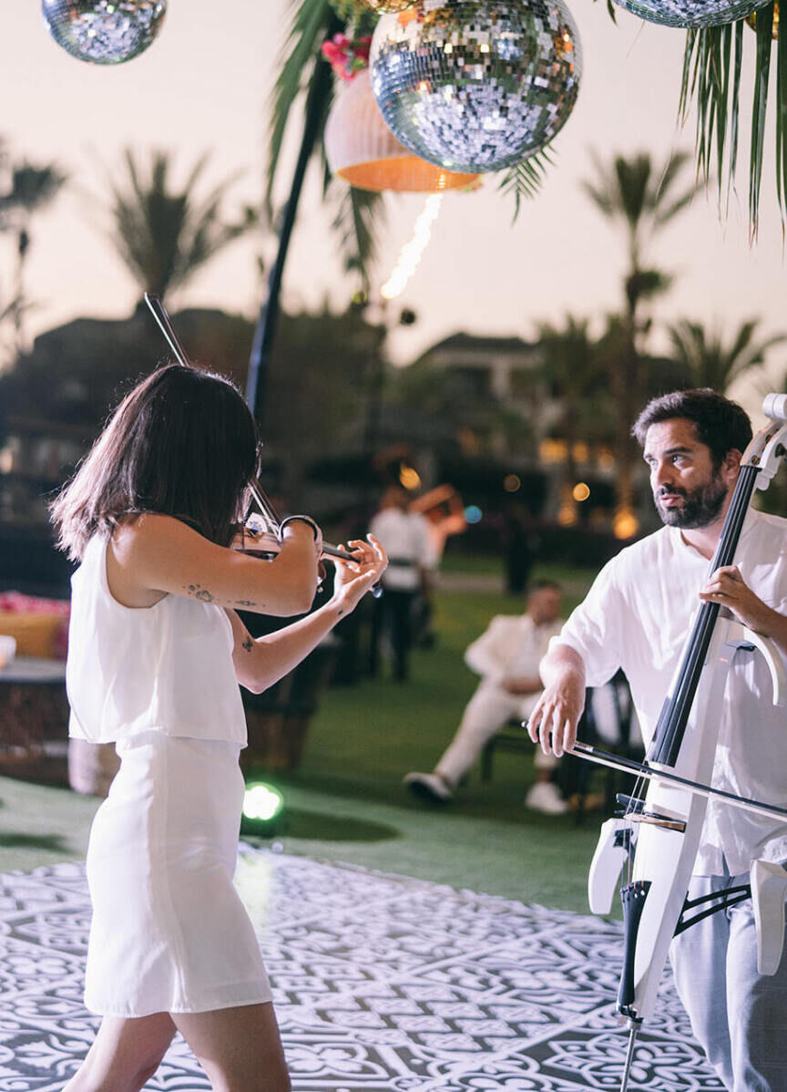 A string duo performs during a glam beach wedding reception in Cabo San Lucas, under a canopy of disco balls.