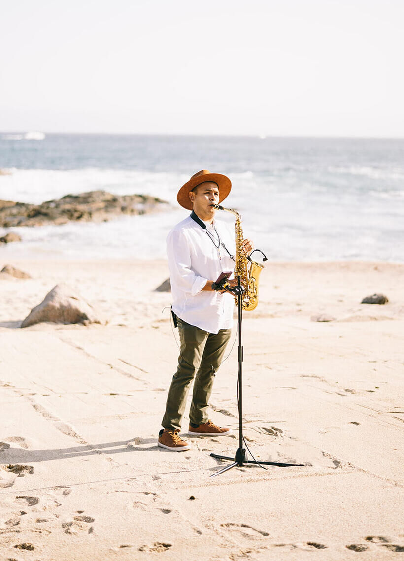 A local saxophonist performs during the waterfront ceremony of a glam beach wedding.