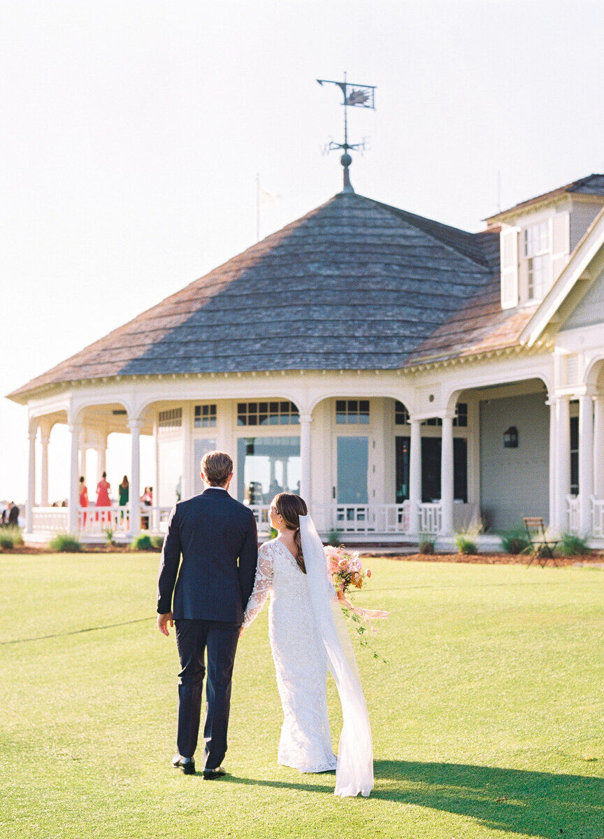 Golf Course Wedding Venues: A couple walking away after their wedding ceremony, approaching a clubhouse with a wraparound porch.