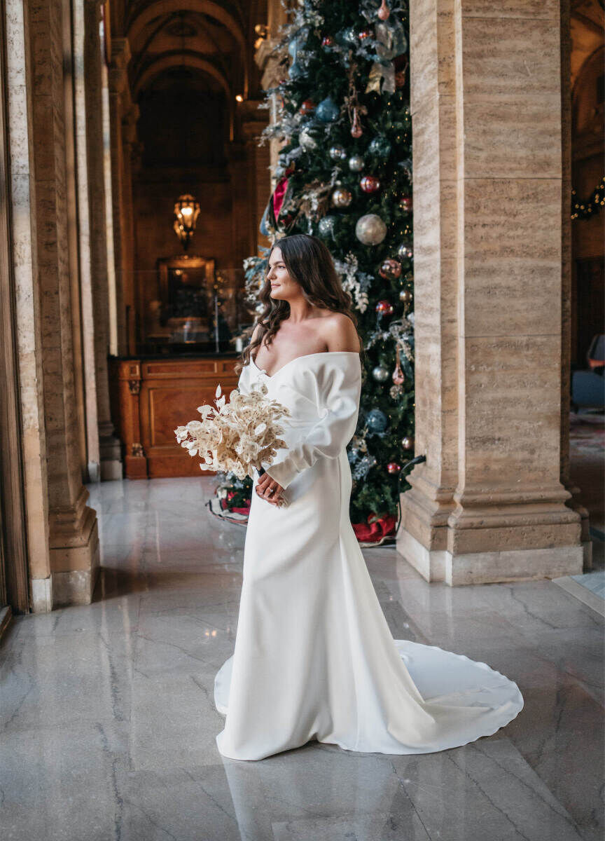 Holiday Wedding: A bride standing and holding a bouquet, with a tall Christmas tree in the background.