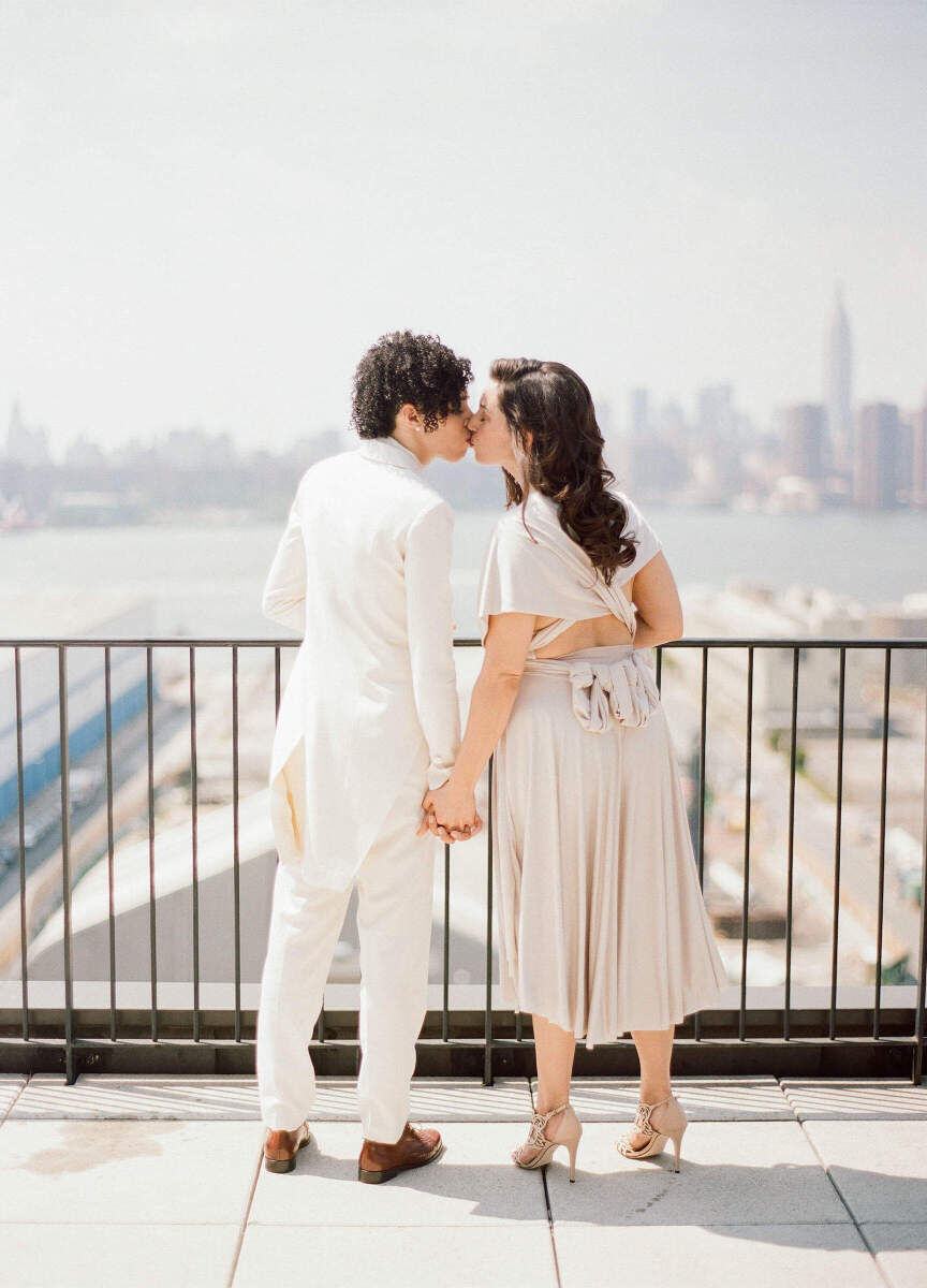 Holiday Wedding: Two newlyweds kissing and holding hands with a city skyline in the background.