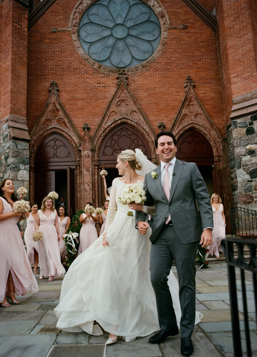 Holiday Wedding: A bride and groom smiling and coming out of a church with their wedding party cheering them on