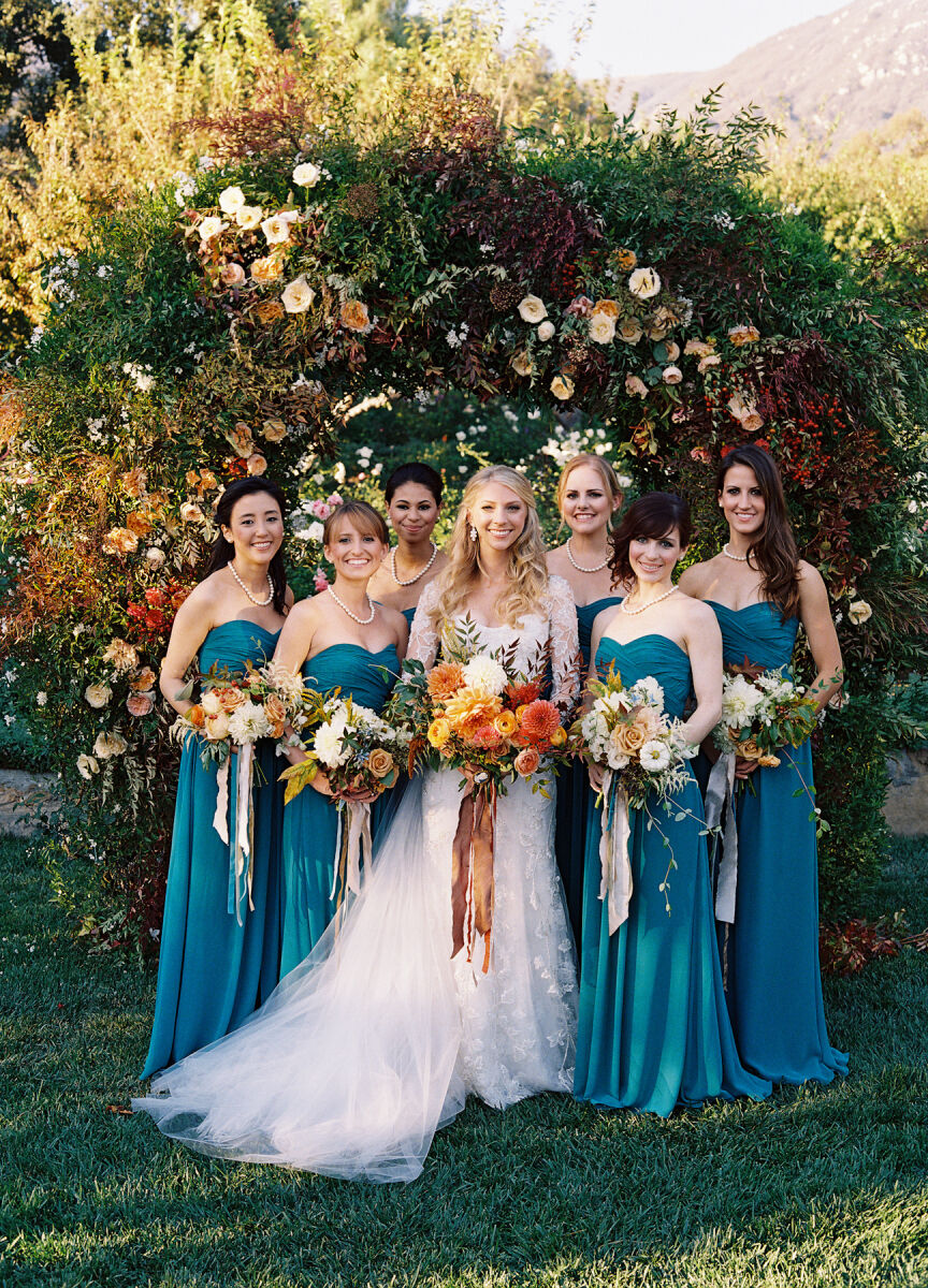 Holiday Wedding: A bride standing with her wedding party against green foliage with fall-inspired florals.