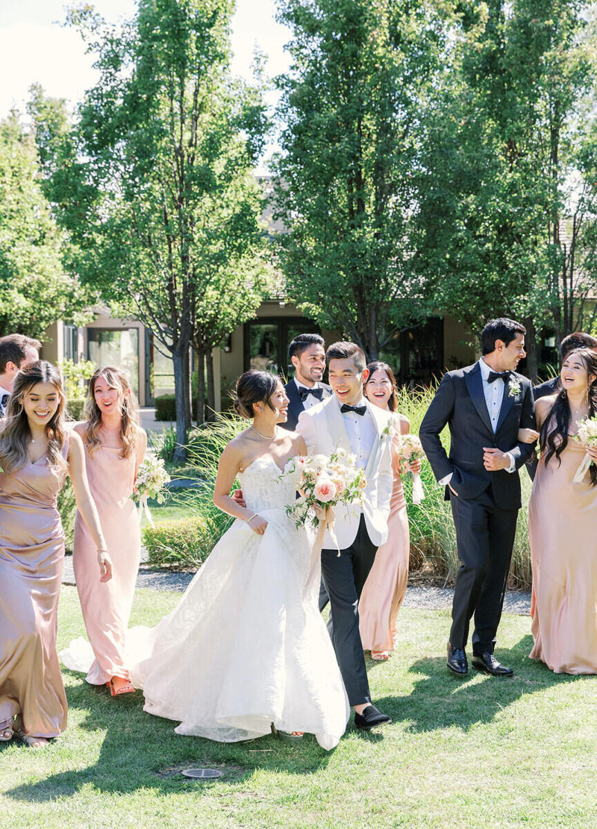 Holiday Wedding: Two newlyweds smiling at each other and walking outside, surrounded by their bridal party.