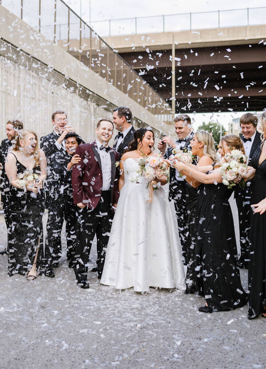 A couple and their wedding party amidst a shower of biodegradable confetti before they went inside for the industrial wedding.